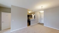 This single-floor residence offers a thoughtfully designed open-concept layout that seamlessly connects the living and kitchen areas, creating a spacious and cohesive environment. The living area features plush carpeted flooring and soft neutral wall tones that contribute to a warm, welcoming ambiance throughout. An elegant pendant light fixture hangs overhead, adding a decorative touch to the space.

The kitchen is positioned adjacent to the living area and is defined by a peninsula-style breakfast bar that acts as both a functional workspace and a natural divider between the two spaces. Dark espresso cabinetry provides a striking contrast against the light countertops, while stainless steel appliances — including a microwave and range — lend a modern, polished feel. Additional pendant lighting above the kitchen area enhances both task visibility and visual appeal.

A tiled entryway near the front door provides a practical transition zone from the exterior into the living space. The open sightlines from the living area through to the kitchen and entry corridor give the residence a sense of depth and flow. Overall, the space balances modern finishes with a neutral, versatile palette, making it a functional and aesthetically cohesive home.