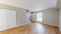 Located at 4373 Bonita Dr in Middletown, Ohio, this two-story home offers a thoughtfully updated interior spread across two floors. The main level features an open living room filled with natural light from a front-facing window, highlighted by warm hardwood-style flooring and neutral gray walls that create a bright, welcoming atmosphere. A staircase with a sleek black metal railing and wood-toned treads leads to the upper level, adding a modern design accent to the entry area. The upper floor houses both bedrooms and a full bathroom, connected by a hallway. Both bedrooms feature the same warm hardwood-style flooring, soft neutral walls, and closets with paneled white doors. Natural light filters in through windows, enhancing the clean, airy feel of each room. The primary bedroom includes a built-in closet and ceiling ventilation. The full bathroom is well-appointed with a tub-shower combination featuring striking marble-look tile surround with a built-in niche, a white vanity with storage, and matching hardwood-style flooring. The cohesive use of neutral tones, updated flooring, and modern fixtures throughout gives this home a fresh, move-in-ready character.