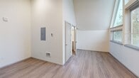 Located in the West Seattle neighborhood at 4124 36th Ave SW, this efficiently designed studio-style unit makes a striking impression with its soaring vaulted ceilings that amplify the sense of space well beyond its compact footprint. The open-concept living area seamlessly combines the living, dining, and kitchen functions into a single, cohesive space. Warm wood-tone luxury vinyl plank flooring runs throughout, complementing the crisp white walls and angled ceiling lines.

The kitchenette is thoughtfully appointed with light gray wood-grain cabinetry, a white tile backsplash, a single-basin sink, an electric cooktop, a microwave, and a full-size stainless steel refrigerator. A tall pantry cabinet provides additional storage. Track lighting overhead and a ventilation fan keep the space functional and bright.

A standout architectural feature is the expansive angled window wall that floods the living area with natural light while offering views of the surrounding tree-lined Seattle neighborhood. Additional windows provide further ventilation and greenery views. The unit also includes a closet, an electrical panel, and a separate bathroom accessible via an interior door, rounding out this practical and modern single-floor residence.