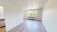 This 2-bedroom, 1-bathroom unit at 318-352 Patricia Ave in Kitchener, Ontario offers a clean, functional layout across a single floor. The open living room features light hardwood flooring, crisp white walls, and a decorative textured ceiling, creating a bright and airy atmosphere. A wide window frames lush, tree-lined street views, with a classic radiator unit beneath providing efficient heating. The separate kitchen is accessed through a clean-cut doorway and is equipped with stainless steel appliances including a full-size refrigerator and dishwasher, complemented by white cabinetry and a tile backsplash. The primary bedroom offers a comfortable footprint, a double-door closet, and access to the hallway connecting the rest of the unit. The second bedroom also benefits from generous natural light through a large window overlooking mature trees. Both bedrooms continue the consistent light hardwood flooring found throughout. The bathroom is finished with classic white subway tile surrounding a full bathtub and shower combination, paired with chrome fixtures for a timeless, clean aesthetic. A connecting hallway ties all rooms together efficiently. The overall design is minimal and well-maintained, offering a bright, move-in ready living space.