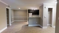 This single-floor space showcases an open-concept design that seamlessly connects the kitchen and living area, creating a cohesive and functional layout. The kitchen is outfitted with dark espresso cabinetry, a stainless steel refrigerator, and a subway tile backsplash that adds a clean, modern touch. A granite-topped breakfast bar serves as a natural dividing element between the kitchen and the living space, offering additional seating and surface area. A track lighting fixture overhead ensures the kitchen is well-lit and practical. The living area is generously proportioned, featuring light hardwood-style flooring that runs throughout the space, lending warmth and continuity. Neutral taupe-toned walls are accented by crisp white crown moulding and baseboards, adding a refined architectural detail. Recessed lighting in the ceiling provides ambient illumination across the open floor plan. The overall ambiance is clean, contemporary, and move-in ready, balancing modern finishes with a welcoming, understated aesthetic well-suited for everyday living.
