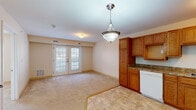 This single-floor residential unit offers a practical and comfortable layout, thoughtfully designed to maximize functionality. The open-concept living and dining area flows seamlessly into the kitchen, creating a welcoming, cohesive space. The living area features neutral-toned carpeting, warm beige walls, and a pendant light fixture, all complemented by a set of French doors that invite natural light and provide access to an outdoor balcony area. The kitchen is well-appointed with warm oak cabinetry extending from floor to ceiling, offering generous storage capacity. Granite-style countertops provide ample prep space, while white appliances — including a refrigerator, electric range, dishwasher, and sink — complete the functional workspace. The tile flooring in the kitchen transitions neatly to the carpeted living area. The bedroom is a quiet, comfortable retreat, featuring plush neutral carpeting, soft beige walls, and a window fitted with blinds that allows natural light while maintaining privacy. The full bathroom is clean and straightforward, finished with tile flooring, a single-sink vanity with oak cabinetry, a wall-mounted mirror, a combination tub and shower with grab bar, and neutral white walls that contribute to a bright, tidy atmosphere throughout.