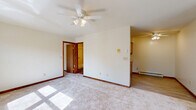 Located at 1949 Western Ave in Albany, NY, this one-bedroom, one-bathroom unit offers a practical and comfortable single-floor layout. The living room is generously sized, featuring plush wall-to-wall carpeting, a ceiling fan with light fixture, large double-pane windows that invite abundant natural light, and a charming arched accent window flanking the entry door. Baseboard heating runs throughout, ensuring efficient warmth year-round. The living area transitions seamlessly into the kitchen, which features hard surface flooring, wood cabinetry, and a functional layout suited for everyday cooking. The bedroom is a comfortable size, with its own ceiling fan, a window overlooking greenery, and direct access to two dedicated closets outfitted with wooden shelving rods for organized storage. The bathroom is cleanly appointed with white tile wainscoting, a mosaic tile floor, and a full tub-shower combination with a chrome grab bar. Warm wood-toned door frames and baseboards provide consistent detailing throughout the unit, lending a cohesive, classic feel to the overall aesthetic. The layout is efficient and well-organized, making thoughtful use of every area within the space.