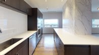This elegant penthouse residence offers two bedrooms and two and a half bathrooms across a generously proportioned single-floor layout, delivering a refined urban living experience. Rich hardwood flooring flows throughout the main living areas, anchoring the home's contemporary aesthetic.

The chef's kitchen is a standout feature, outfitted with dark espresso cabinetry, crisp white quartz countertops, stainless steel appliances including double wall ovens, and a dramatic marble-clad accent wall. A second kitchen configuration mirrors the same high-end cabinetry and finishes, offering exceptional functionality.

The primary bedroom suite is bathed in natural light from wide horizontal windows with sweeping city views, complemented by a ceiling fan and generous proportions. It connects to a spa-caliber ensuite bathroom appointed with mosaic marble tile flooring, a freestanding soaking tub, a glass-enclosed rain shower, and an illuminated vanity mirror. A spacious walk-in closet with floor-to-ceiling adjustable shelving and hanging systems provides abundant storage.

The second bedroom is equally well-appointed with hardwood floors and an elegant multi-bulb pendant light fixture. A stylish secondary full bathroom echoes the same refined material palette. The powder room features a striking pedestal sink and floor-to-ceiling tile work, adding a bold design moment.
