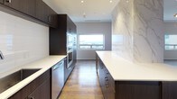 This elegant penthouse residence offers two bedrooms and two and a half bathrooms across a generously proportioned single-floor layout, delivering a refined urban living experience. Rich hardwood flooring flows throughout the main living areas, anchoring the home's contemporary aesthetic.

The chef's kitchen is a standout feature, outfitted with dark espresso cabinetry, crisp white quartz countertops, stainless steel appliances including double wall ovens, and a dramatic marble-clad accent wall. A second kitchen configuration mirrors the same high-end cabinetry and finishes, offering exceptional functionality.

The primary bedroom suite is bathed in natural light from wide horizontal windows with sweeping city views, complemented by a ceiling fan and generous proportions. It connects to a spa-caliber ensuite bathroom appointed with mosaic marble tile flooring, a freestanding soaking tub, a glass-enclosed rain shower, and an illuminated vanity mirror. A spacious walk-in closet with floor-to-ceiling adjustable shelving and hanging systems provides abundant storage.

The second bedroom is equally well-appointed with hardwood floors and an elegant multi-bulb pendant light fixture. A stylish secondary full bathroom echoes the same refined material palette. The powder room features a striking pedestal sink and floor-to-ceiling tile work, adding a bold design moment.