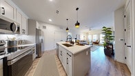 This thoughtfully designed 2-bedroom, 2-bathroom residence offers a seamless open-concept layout connecting the kitchen, dining, and living areas. The kitchen is a standout feature, equipped with stainless steel appliances including a full-size refrigerator, range, microwave, and dishwasher. Gray shaker-style cabinetry with matte black hardware pairs with white quartz countertops and a subway tile backsplash. A central island with an undermount sink and pendant lighting above provides both additional prep space and casual bar seating. Light wood-look flooring flows throughout the main living areas, complementing the bright, neutral color palette. The living room receives ample natural light through large windows and a sliding glass door, and features a ceiling fan overhead. Both bedrooms are carpeted and generously sized, with the primary bedroom offering comfortable proportions and access to its own bathroom. The bathrooms are finished with white quartz vanity tops, gray cabinetry, and matte black fixtures. Two hallways connect the space efficiently, contributing to a practical and functional floor plan throughout this well-balanced single-story home.