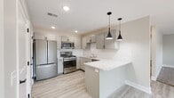 Located at 1976 RW Berends Dr SW in Wyoming, MI, this thoughtfully designed single-floor unit offers a clean, modern aesthetic with high-quality finishes throughout. The kitchen is a standout feature, showcasing gray shaker-style cabinetry, a white subway tile backsplash, light granite countertops, and a full suite of stainless steel appliances including a gas range, over-the-range microwave, and French door refrigerator. A peninsula with pendant lighting in matte black provides additional counter space and a casual dining area, while light-toned luxury vinyl plank flooring ties the space together seamlessly. The open living area is bright and airy, with recessed lighting, large sliding glass doors fitted with vertical blinds, and windows that allow natural light to fill the room. A transition from hard flooring to plush neutral carpet defines the living zone. The bedrooms are comfortably sized, carpeted, and feature windows with outdoor views and ample closet space. The bathroom is finished with a shaker-style vanity, granite countertop, matte black hardware, a large mirror, and a shower-tub combination. Throughout the unit, neutral gray walls, white trim, and consistent modern fixtures create a cohesive and inviting atmosphere.