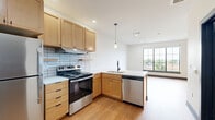 This studio apartment on the fifth floor at 320 S Shelby St in Louisville, Kentucky, offers a thoughtfully designed, single-level layout that maximizes every square foot. The open-concept living area features light hardwood flooring, crisp white walls, and bold dark baseboards that provide a clean, modern contrast. Large, grid-paned windows flood the space with natural light and frame views of the surrounding Louisville cityscape and tree canopy, creating an airy, connected atmosphere. A ceiling fan adds comfort and functionality to the living area.

The kitchen is well-appointed with warm-toned maple cabinetry, light countertops, and a classic subway tile backsplash. Stainless steel appliances — including a refrigerator, electric range, and dishwasher — provide a sleek, contemporary finish, while a pendant light above the sink adds a stylish touch. Ample upper and lower cabinetry, along with a tall pantry unit, offer generous storage.

The bathroom features distinctive large-format hexagonal tile flooring in charcoal gray, a maple vanity with a white countertop, and wall-mounted lighting flanking a framed mirror, delivering a clean and modern aesthetic. The unit also includes a dedicated closet and in-unit laundry, enhancing everyday convenience throughout this efficiently planned downtown Louisville residence.