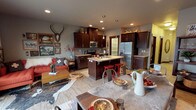 Located in Spokane, WA, this three-floor home blends rustic charm with modern functionality throughout its well-designed layout. The main level showcases an open-concept living, dining, and kitchen area bathed in natural light from sliding glass doors that lead to an outdoor balcony. The kitchen is outfitted with rich dark cabinetry, granite countertops, stainless steel appliances, a walk-in pantry, and a central island with bar seating — ideal for both cooking and casual entertaining. The adjoining dining area features hardwood-style flooring and carries a nature-inspired aesthetic with eclectic décor accents. A dedicated laundry room with overhead cabinetry adds practical convenience. Upstairs, a private office with neighborhood views provides a quiet workspace, while a cozy bedroom with wooded views offers a serene retreat. A well-appointed bathroom with dark vanity cabinetry and ample lighting serves the upper level. The lower level features a spacious family room with recessed lighting and a comfortable lounge setup, perfect for relaxing or entertaining. Throughout the home, a cohesive warm-toned, nature-inspired design palette ties each floor together, creating an inviting and functional living environment.