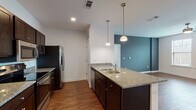 This 2-bedroom, 2-bathroom residence in Lakeland, Tennessee is a single-floor unit thoughtfully designed with modern finishes and a cohesive aesthetic. The open-concept kitchen flows seamlessly into the living area and features dark espresso cabinetry, granite countertops, a double-basin sink set in a central island, stainless steel appliances including a French door refrigerator, range, microwave, and dishwasher, and elegant pendant lighting overhead. Rich hardwood-style flooring runs throughout the entire unit, adding warmth and continuity.

The living area is highlighted by a bold teal accent wall, a ceiling fan, and natural light from a large window, creating an inviting and comfortable atmosphere. Both bedrooms are generously proportioned, with one featuring a ceiling fan, a walk-in closet, and direct access to an en-suite bathroom. The second bedroom offers a bright window with exterior views and ample floor space. Each bathroom is finished with granite-topped dark wood vanities and a tub/shower combination. The clean, neutral palette and consistent finishes throughout lend the space a polished, move-in-ready appeal well suited for modern living in Lakeland, TN.