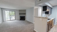 This well-appointed 2-bedroom, 2-bathroom single-floor residence offers a thoughtfully designed layout encompassing a comfortable amount of living space. The open living room serves as the heart of the home, featuring plush carpeting, neutral gray walls, a textured ceiling, and a sleek black fireplace with a matching mantel as a central focal point. A sliding glass door floods the room with natural light and opens onto a covered wooden balcony overlooking mature trees, providing a peaceful outdoor retreat. The galley-style kitchen is efficiently designed with dark espresso cabinetry, granite-look countertops, light hardwood-style flooring, and stainless steel appliances, with a pass-through bar connecting it to the living area. A dedicated utility room with laundry hookups is accessible directly from the kitchen. The primary bedroom is generously sized with plush carpet, a ceiling fan, and a private en suite bathroom featuring a soaking jetted tub with tiled surround. The second bedroom offers bright natural light through a large window with views of surrounding greenery. The second full bathroom includes a tub/shower combo, wood-look flooring, dark wood vanity, and granite-topped counters. Two closets provide ample storage throughout the unit.