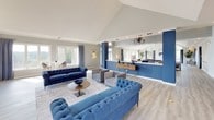 The Park Hoover Clubhouse is a thoughtfully designed single-story community space that blends contemporary style with a welcoming atmosphere. The interior is defined by soaring vaulted ceilings and light gray walls accented by bold navy blue columns and feature walls, creating a cohesive and sophisticated color palette throughout.

The expansive main gathering area is anchored by multiple seating zones, including tufted navy Chesterfield sofas, gray accent chairs, and gold-toned coffee tables arranged atop textured area rugs over light wood-look flooring. Recessed lighting and a chandelier provide warm illumination, complementing the generous natural light streaming through large windows dressed with soft gray drape panels.

A prominent central bar counter with a white surface and navy base accommodates several bar-height stools, making it an ideal hub for social gatherings. Beyond the bar, a fireplace serves as a focal point flanked by additional seating and decorative furnishings.

One of the clubhouse's standout features is a windowed nook offering panoramic views of the outdoor pool and sundeck, lined with lounge chairs and surrounded by mature trees. This connection to the outdoor amenity space enhances the overall ambiance, making the Park Hoover Clubhouse a versatile and inviting venue for residents.