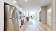 This single-floor residence showcases a thoughtfully designed open-concept layout that seamlessly connects the kitchen, dining, and living areas. The kitchen is well-appointed with white shaker cabinetry, a subway tile backsplash, stainless steel appliances including a refrigerator, range, microwave, and dishwasher, all set against light hardwood flooring that extends throughout the unit. Recessed lighting illuminates the space evenly, complementing the bright, neutral palette.

The living area is anchored by a large picture window that floods the room with natural light and offers outdoor views, creating an open and airy atmosphere. The dining space sits naturally between the kitchen and living room, making the layout ideal for both everyday living and entertaining.

Two well-proportioned bedrooms each feature hardwood flooring, recessed lighting, closet storage, and windows that bring in natural light. Both bathrooms are finished with striking marble-look tile on both the floors and shower surrounds, paired with modern wall-mounted toilets, lending a clean and upscale aesthetic. The overall design of the unit is cohesive, modern, and light-filled throughout.