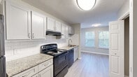 Located at 1238 Mill Crest Walk NW in Conyers, Georgia, this single-floor home offers four bedrooms, two bathrooms, and a notably unique dual-kitchen layout. The kitchens are well-appointed with white and gray shaker-style cabinetry, granite-look countertops, white subway tile backsplashes, black appliances including electric ranges and dishwashers, and durable light-tone luxury vinyl plank flooring. Natural light filters in through windows fitted with horizontal blinds, creating a bright and functional cooking and dining environment. The bedrooms feature soft carpeting in neutral tones, with walls painted in a warm greige palette that lends a calm, cohesive ambiance throughout. The spacious primary bedroom includes closet storage with built-in hanging rods, while additional bedrooms offer comparable comfort and natural light. Both bathrooms are finished with granite-topped vanities, white cabinetry, tub-shower combinations, and neutral tile flooring, maintaining a clean and consistent aesthetic. Textured ceilings and white trim carry through the entire home, contributing to a polished, uniform look. The layout, as seen in the 3D overview, is efficient and well-organized, making this a practical and comfortable home suited for a variety of living needs.