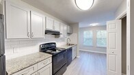 Located at 1238 Mill Crest Walk NW in Conyers, Georgia, this single-floor home offers four bedrooms, two bathrooms, and a notably unique dual-kitchen layout. The kitchens are well-appointed with white and gray shaker-style cabinetry, granite-look countertops, white subway tile backsplashes, black appliances including electric ranges and dishwashers, and durable light-tone luxury vinyl plank flooring. Natural light filters in through windows fitted with horizontal blinds, creating a bright and functional cooking and dining environment. The bedrooms feature soft carpeting in neutral tones, with walls painted in a warm greige palette that lends a calm, cohesive ambiance throughout. The spacious primary bedroom includes closet storage with built-in hanging rods, while additional bedrooms offer comparable comfort and natural light. Both bathrooms are finished with granite-topped vanities, white cabinetry, tub-shower combinations, and neutral tile flooring, maintaining a clean and consistent aesthetic. Textured ceilings and white trim carry through the entire home, contributing to a polished, uniform look. The layout, as seen in the 3D overview, is efficient and well-organized, making this a practical and comfortable home suited for a variety of living needs.