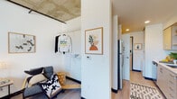This thoughtfully designed single-floor unit blends modern style with industrial character, evident in the exposed concrete ceilings that contrast beautifully with crisp white walls and warm wood-look flooring throughout. The kitchen is efficiently laid out with sleek light-wood cabinetry, stainless steel appliances including a refrigerator, electric range, and microwave, plus generous counter space and ample storage — ideal for everyday cooking. Adjacent to the kitchen is a multifunctional living area that features an open clothes rack and in-unit washer, maximizing utility within a compact footprint. The bedroom is a bright, restful retreat with a large window that invites abundant natural light and views of the surrounding greenery. A separate study or flex room also benefits from a large window with urban views, a wall-mounted HVAC unit, and enough space for a full home office setup. The bathroom is clean and contemporary, featuring a white quartz vanity, wood-toned cabinetry, a large mirror, and a shower-tub combo. Consistent warm-toned lighting, light hardwood flooring, and a cohesive modern palette tie the entire space together, creating a functional and welcoming living environment.