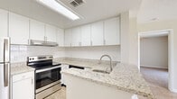 This well-designed one-bedroom, one-bathroom unit offers an efficient single-floor layout that maximizes every square foot of its compact footprint. The kitchen serves as a standout feature, showcasing granite countertops with subtle grey and white veining, a peninsula with an undermount sink and pull-down faucet, and a full suite of stainless steel appliances including a refrigerator, electric range, and dishwasher. Crisp white cabinetry extends to the ceiling, providing generous storage, while a skylight panel overhead floods the space with natural light. Light wood-style flooring runs throughout the kitchen and entry areas, enhancing the clean, contemporary aesthetic.

The bedroom is carpeted for comfort and features a sliding glass door dressed with vertical blinds, offering views of outdoor greenery and providing direct access to the exterior. A ceiling fan with integrated lighting adds functionality to the room. The bathroom maintains the unit's clean palette with white cabinetry, a large vanity mirror with overhead lighting, a full soaking tub with shower, and matching wood-style flooring. Overall, the unit presents a bright, modern atmosphere with cohesive finishes throughout.