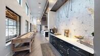 This expansive single-floor amenity space is designed to impress, offering a thoughtfully curated mix of social, recreational, and professional areas. The main living lounge commands attention with its soaring double-height ceilings, floor-to-ceiling windows, and an abundance of natural light. Geometric linear lighting accents the ceiling above plush seating arrangements in soft grays and teals, creating an inviting atmosphere. A built-in wet bar with bar seating and a wall-mounted television anchors the entertaining area. Adjacent to the lounge, the kitchenette features dark navy cabinetry with sleek hardware, marble-look countertops, and a striking geometric patterned accent wall, complemented by pendant lighting. The game room is a standout, housing a full-size billiard table beneath soaring ceilings, a shuffleboard table, and a vibrant teal vertical slat feature wall, all bathed in natural light from oversized windows. A dedicated co-working area includes a marble-topped communal table with ergonomic seating, a wall-mounted display, and designer pendant lighting. Private focus rooms with frosted glass doors and exterior views offer quiet workspaces. Wide-plank hardwood flooring flows throughout, tying all areas together with a cohesive, modern aesthetic.