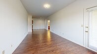 This single-floor residence offers a cohesive and functional layout, unified throughout by warm, rich hardwood-style flooring that lends a sense of continuity and warmth to every room. The open living area is generously sized, bathed in natural light through large windows fitted with horizontal blinds, and features clean white walls that create a bright, neutral canvas adaptable to a variety of interior styles.

The galley-style kitchen is well-equipped, featuring warm oak cabinetry with ample upper and lower storage, dark countertops, a double-basin sink, and a suite of stainless steel appliances including a gas range, over-the-range microwave, dishwasher, and refrigerator. Recessed lighting overhead enhances the kitchen's functionality. A door at the end of the kitchen provides convenient additional access.

Multiple bedrooms are present throughout the unit, each finished with the same hardwood-style flooring and crisp white walls. Several rooms benefit from windows that invite natural light and provide outdoor views, while panel-style doors with brass hardware add a classic touch. The bathroom includes a vanity with warm wood cabinetry, a light countertop, and a separate water closet area with a toilet and towel bar. The overall ambiance of the space is clean, practical, and move-in ready.