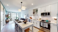 This thoughtfully designed single-floor residence blends contemporary finishes with warm, inviting character throughout. The open-concept kitchen is a standout feature, showcasing crisp white shaker cabinetry with black hardware, a herringbone-patterned tile backsplash, quartz countertops, and a full suite of stainless steel appliances. A central island with bar seating serves as both a prep space and casual dining area, illuminated by modern pendant lighting. The kitchen flows seamlessly into the living area, where oversized black-framed windows flood the space with natural light and frame panoramic urban skyline views. The living room offers a relaxed yet refined atmosphere, with ample room for both a seating arrangement and a reading nook. Both bedrooms feature warm hardwood flooring, large windows with city views, and clean, neutral walls that create a calm retreat. The primary bathroom is particularly distinctive, with bold navy cabinetry, a dual-sink vanity with white countertops, a classic black-and-white mosaic tile floor, a glass-enclosed walk-in shower with subway tile surround, and direct access to a well-organized walk-in closet. Throughout the residence, hardwood floors, recessed lighting, and a cohesive modern aesthetic create a polished and comfortable living environment.