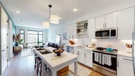 This thoughtfully designed single-floor residence blends contemporary finishes with warm, inviting character throughout. The open-concept kitchen is a standout feature, showcasing crisp white shaker cabinetry with black hardware, a herringbone-patterned tile backsplash, quartz countertops, and a full suite of stainless steel appliances. A central island with bar seating serves as both a prep space and casual dining area, illuminated by modern pendant lighting. The kitchen flows seamlessly into the living area, where oversized black-framed windows flood the space with natural light and frame panoramic urban skyline views. The living room offers a relaxed yet refined atmosphere, with ample room for both a seating arrangement and a reading nook. Both bedrooms feature warm hardwood flooring, large windows with city views, and clean, neutral walls that create a calm retreat. The primary bathroom is particularly distinctive, with bold navy cabinetry, a dual-sink vanity with white countertops, a classic black-and-white mosaic tile floor, a glass-enclosed walk-in shower with subway tile surround, and direct access to a well-organized walk-in closet. Throughout the residence, hardwood floors, recessed lighting, and a cohesive modern aesthetic create a polished and comfortable living environment.
