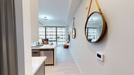 Located at 220 Meridian in the heart of downtown Indianapolis, this contemporary one-bedroom, one-bathroom residence offers a thoughtfully designed open-concept layout with modern finishes throughout. Light wood-style flooring flows across the single level, complementing the clean, neutral color palette that defines the space.

The open living and kitchen area serves as the centerpiece of the home. The kitchen is outfitted with stainless steel appliances, crisp white cabinetry, a sleek white quartz waterfall island with an undermount sink and bar seating, and statement linear pendant lighting overhead — combining both style and functionality. The living area is anchored by dramatic floor-to-ceiling windows that frame sweeping views of the Indianapolis skyline, flooding the space with abundant natural light.

The bedroom offers a well-proportioned retreat, featuring a ceiling fan, access to a walk-in closet, and a calm, softly lit ambiance with a neutral palette. The bathroom is finished with large-format marble-style tile flooring, a warm wood vanity with ample storage, a backlit mirror, and a clean, spa-inspired aesthetic.

Throughout the residence, bold dark door frames and gold accent fixtures provide striking contrast against the bright white walls, lending the space a polished, upscale urban character.
