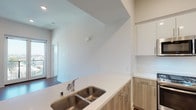 This well-appointed single-floor residence offers a clean, contemporary design highlighted by rich hardwood-style flooring that extends throughout every room. The open-concept layout seamlessly connects the living area to the kitchen, which serves as the heart of the home. The kitchen is equipped with a full suite of stainless steel appliances, including a gas range, over-the-range microwave, and refrigerator. Two-toned cabinetry pairs light wood lower cabinets with crisp white upper cabinets, complemented by white quartz countertops and a double basin undermount sink. A peninsula counter provides additional workspace and casual dining potential.

The living area is bright and spacious, benefiting from recessed lighting and access to a private balcony through glass French doors, offering pleasant outdoor views. The bedrooms are generously sized with clean white walls, large closets, and ample natural light. Both bathrooms are finished in a consistent, modern aesthetic — one featuring a full soaking tub and tiled shower surround, the other a glass-enclosed walk-in shower with tiled walls and chrome fixtures. The overall ambiance is fresh, neutral, and move-in ready, reflecting a thoughtfully designed contemporary living space.