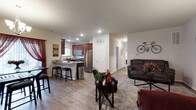 Unit 803 is a single-floor residence designed with an open-concept floor plan that creates a seamless flow between the main living spaces. The kitchen is outfitted with rich, dark wood cabinetry, stainless steel appliances including a refrigerator, microwave, and range, and is anchored by a peninsula countertop with bar seating — ideal for casual dining or entertaining. The kitchen transitions naturally into the living area, which features durable wood-look flooring, recessed lighting, and neutral walls that provide a clean, versatile backdrop. The living space offers ample room for comfortable seating arrangements, highlighted by a plush area rug that defines the gathering area. A hallway leads to additional rooms beyond, suggesting a thoughtful layout that balances open communal spaces with private retreats. Throughout the residence, the consistent flooring, coordinated finishes, and practical design choices reflect a well-appointed interior. The overall ambiance is warm and welcoming, combining functional design with modern aesthetic details that make the space both livable and visually appealing.