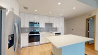 Located at 1001 NE Baker Rd in Stuart, Florida, this single-floor residence showcases a clean, contemporary design with a cohesive neutral palette and light wood-tone flooring carried throughout. The open-concept kitchen serves as a central highlight, equipped with stainless steel appliances including a range, microwave, dishwasher, and refrigerator. Crisp white shaker-style cabinetry extends to the ceiling for maximum storage, complemented by a subtle gray tile backsplash and a bright white countertop island that provides additional workspace and casual seating potential. Recessed lighting illuminates the kitchen efficiently.

The living and bedroom areas offer generous proportions, with light-filled rooms benefiting from windows fitted with blinds and, in one room, direct access to a private balcony with outdoor views. Ceiling fans are installed in select rooms, adding comfort. Closets feature wire shelving systems, and at least one walk-in closet offers expanded storage capacity.

The bathroom is finished with marble-look tile flooring, a dual-sink white vanity with a warm wood-framed mirror, and modern chrome fixtures, contributing to the space's overall polished, move-in-ready aesthetic. A hallway with louvered closet doors provides additional storage convenience.