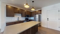 Located at 500 W Broad St in the heart of Columbus, Ohio, this single-floor residence blends modern design with thoughtful functionality. The open-concept kitchen serves as the centerpiece of the living area, showcasing rich dark-stained cabinetry, quartz countertops, and a classic white subway tile backsplash. Stainless steel appliances, a matte black faucet, and stylish pendant lighting add refined detail, while a central island provides additional prep and gathering space. Warm hardwood-style flooring flows throughout the main living areas, complementing the clean, contemporary aesthetic. The living space opens to the outdoors through French doors, allowing an abundance of natural light to fill the room. Bedrooms are generously proportioned, finished with plush carpet and large windows that frame views of the surrounding urban landscape. The primary bathroom features a dual-sink vanity with dark cabinetry, quartz countertops, matte black fixtures, and a tiled walk-in shower, with a walk-in closet conveniently adjacent. A secondary bathroom mirrors the same quality finishes. Throughout the residence, crisp white walls, recessed lighting, and matte black hardware create a cohesive, modern sensibility that suits contemporary urban living.