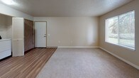 This single-floor residence offers a practical and well-organized layout across its living spaces. The open living area serves as the heart of the unit, featuring a combination of plush carpeting and wood-look hard flooring that transitions naturally between zones. A pass-through opening connects the living space to the kitchen area, enhancing the sense of openness. Natural light filters in through a window fitted with blinds, offering views of surrounding greenery.

The galley-style kitchen is efficiently arranged with countertops lining both sides, white cabinetry above and below, and includes appliances such as a stainless steel refrigerator and a dishwasher. The layout maximizes storage and workflow within a compact footprint.

The bedroom is a quiet, carpeted space bathed in natural light from a window overlooking outdoor foliage. Its textured ceiling and neutral wall tones create a calm, understated atmosphere.

The bathroom is equipped with a single-basin vanity featuring a laminate countertop, ample cabinet storage below, and a full-width mirror above. A combined tub and shower with a curved curtain rod and safety grab bars completes the space, finished with wood-look flooring. An in-unit laundry area is also present, adding everyday convenience to the overall layout.