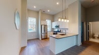 Located at Farrell Communities at Islip along Sunburst and Eastview Drives in Central Islip, NY, this single-floor residence offers a thoughtfully designed layout with modern finishes throughout. The open-concept kitchen is a standout feature, boasting white shaker-style cabinetry, stainless steel appliances including a gas range, microwave, and French door refrigerator, as well as a central island with an integrated sink and pendant lighting overhead. Soaring ceilings and tall double-hung windows flood the kitchen and adjacent living areas with abundant natural light and views of the surrounding community. Durable light wood-tone flooring runs seamlessly throughout the living and bedroom spaces, contributing to a clean, cohesive aesthetic. The bedrooms are generously proportioned with neutral tones, high ceilings, and windows that bring in additional natural light. The bathroom is finished to a high standard, featuring marble-look porcelain tile flooring, gray shaker-style vanity cabinetry with white quartz countertops, and a tub and shower combination accented with gray subway tile. Recessed lighting and a large mirror complete the polished look. Overall, the space presents a contemporary, move-in-ready environment with quality materials and bright, open interiors.