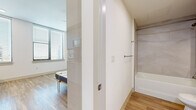 Located at 800 N 2nd St in downtown Phoenix, Arizona, this efficiently designed studio offers a thoughtful single-floor layout that maximizes every square foot. Light wood-tone flooring flows consistently throughout, creating a cohesive and airy aesthetic across the entire space.

The kitchen is a standout feature, showcasing crisp white cabinetry, a bold navy herringbone tile backsplash, white countertops, and stainless steel appliances including an over-the-range microwave and dishwasher. A built-in desk area extends from the kitchen counter, adding a practical workspace without sacrificing style.

The main living area is bright and open, with large windows fitted with horizontal blinds that invite generous natural light and offer views of the surrounding Phoenix cityscape. A built-in Murphy bed system with an upholstered blue headboard and integrated shelving units provides flexible, space-saving sleeping arrangements while maintaining an organized, uncluttered environment.

The bathroom is clean and functional, featuring wood-look flooring, a full soaking tub with tile surround, a white vanity with under-cabinet storage, and brushed nickel hardware and towel bars throughout. The overall design aesthetic is modern and minimalist, emphasizing clean lines, neutral tones, and smart use of space.