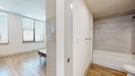 Located at 800 N 2nd St in downtown Phoenix, Arizona, this efficiently designed studio offers a thoughtful single-floor layout that maximizes every square foot. Light wood-tone flooring flows consistently throughout, creating a cohesive and airy aesthetic across the entire space.

The kitchen is a standout feature, showcasing crisp white cabinetry, a bold navy herringbone tile backsplash, white countertops, and stainless steel appliances including an over-the-range microwave and dishwasher. A built-in desk area extends from the kitchen counter, adding a practical workspace without sacrificing style.

The main living area is bright and open, with large windows fitted with horizontal blinds that invite generous natural light and offer views of the surrounding Phoenix cityscape. A built-in Murphy bed system with an upholstered blue headboard and integrated shelving units provides flexible, space-saving sleeping arrangements while maintaining an organized, uncluttered environment.

The bathroom is clean and functional, featuring wood-look flooring, a full soaking tub with tile surround, a white vanity with under-cabinet storage, and brushed nickel hardware and towel bars throughout. The overall design aesthetic is modern and minimalist, emphasizing clean lines, neutral tones, and smart use of space.