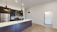 Located at 1050 N. 4th St in Columbus, Ohio's vibrant Short North area, this modern single-floor residence offers a thoughtfully designed open-concept layout with contemporary finishes throughout. The kitchen serves as the heart of the space, showcasing a large center island with a crisp white countertop, an undermount sink, and bold matte black pendant lighting that hangs from soaring ceilings. Dark espresso cabinetry lines the walls, complemented by a decorative tile backsplash and a full suite of stainless steel appliances, including a refrigerator, range, and built-in microwave. Light-toned hardwood flooring flows seamlessly throughout the entire unit, enhancing the airy, cohesive feel. The bedrooms are bright and generously proportioned, with large black-framed windows that frame views of the surrounding greenery and neighborhood. The bathrooms are finished with distinctive slate-gray subway tile, large-format white floor tiles, sleek vanities with marble-style countertops, and frameless glass shower enclosures. Recessed lighting and clean white walls contribute to a crisp, modern ambiance throughout, making this a well-appointed and move-in-ready space in the heart of Columbus.