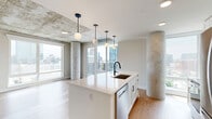 Located in Nashville's vibrant Midtown neighborhood, this two-bedroom, two-bathroom residence offers a striking blend of industrial and modern design. Exposed concrete ceilings and structural columns run throughout the space, complemented by light hardwood flooring in the main living areas and plush carpet in the bedrooms, creating a dynamic contrast of textures.

The open-concept living, dining, and kitchen area serves as the heart of the home. The kitchen features a central island with a white quartz countertop, a matte black faucet with an undermount sink, white cabinetry, stainless steel appliances, and stylish globe pendant lights suspended from the concrete ceiling. Expansive floor-to-ceiling windows and direct balcony access flood the space with natural light and frame sweeping views of the Nashville skyline.

Both bedrooms are generously sized, with large windows offering impressive city views and concrete columns adding architectural character. Each bedroom connects to its own bathroom — one featuring a soaking tub and the other a well-appointed vanity with white quartz counters and matte black fixtures. Three closets provide ample storage throughout. A dedicated laundry area and a hallway with an electrical panel add practical functionality. The balcony offers an ideal outdoor retreat with panoramic urban views.
