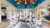 This expansive residential community clubhouse offers a thoughtfully designed, multi-functional layout spanning a generous single floor. The centerpiece is a striking lounge area distinguished by soaring ceilings painted in a bold teal, accented by exposed rustic wood beam trusses and a dramatic oversized pendant light. Plush neutral seating, gold-accented furnishings, and abstract art create an inviting, upscale atmosphere with natural light filtering through large windows dressed in patterned drapes.

Adjacent to the lounge, a modern catering kitchen features a waterfall-edge marble island with bar seating, industrial open shelving with wood backings, pendant lighting, and polished concrete floors — ideal for gatherings and events. The leasing office area presents a professional yet welcoming aesthetic, with patterned wallcovering, bold globe pendant fixtures, and vibrant blue accent chairs set before a sleek reception desk.

A dedicated conference room offers a long dark dining-style table, ample seating, and a large illuminated wall feature. The fitness center is well-equipped with free weights, cable machines, and cardio equipment. Outdoors, a resort-style pool with lounge chairs and pergolas overlooks the broader community. A dedicated mail and package locker corridor rounds out the practical amenities of this well-appointed facility.