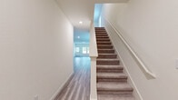 This two-story home presents a cohesive, contemporary design defined by neutral tones, clean lines, and a consistent use of materials throughout. The main level features wood-look plank flooring that extends from the entry hallway through the open-concept living area and kitchen, creating a seamless, airy flow. The living area is generously proportioned, with recessed lighting and a window that invites natural light and outdoor views.

The kitchen is well-appointed with white shaker-style cabinetry, granite countertops with subtle veining, a central island with an undermount sink, and a full suite of stainless steel appliances including a refrigerator, range, microwave, and dishwasher. A secondary bathroom on the main level features wood-look tile flooring, a white vanity, and a tub-shower combination.

A carpeted staircase with a white handrail connects both floors. Upstairs, bedrooms feature plush carpet and windows that provide natural light. The primary bathroom includes a wide white shaker vanity, a large mirror with a lighted fixture, wood-look tile flooring, and access to a spacious walk-in closet fitted with built-in shelving and hanging rods. The overall ambiance is bright, clean, and move-in ready.