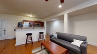 This single-floor unit offers a well-organized layout that balances open communal spaces with private quarters. The heart of the unit is an open-concept living and kitchen area, where warm hardwood floors run continuously throughout, lending a cohesive and inviting feel. The kitchen is equipped with stainless steel appliances, including a microwave, electric range, and refrigerator, all complemented by rich dark wood cabinetry and granite-style countertops. A peninsula counter with bar seating for two provides a convenient dining or casual workspace option. The adjacent living area features a ceiling fan, recessed lighting, and windows positioned near the ceiling that draw in natural light, creating an airy atmosphere despite the below-grade setting. Three bedrooms are each finished with the same hardwood flooring and are served by windows that allow in natural light. The rooms offer comfortable proportions suitable for a bed and supporting furniture. The full bathroom includes a tiled tub-shower combination, a vanity with storage, and tile flooring. Throughout the unit, the neutral color palette on the walls and consistent flooring choices contribute to a clean, functional, and unified living environment.