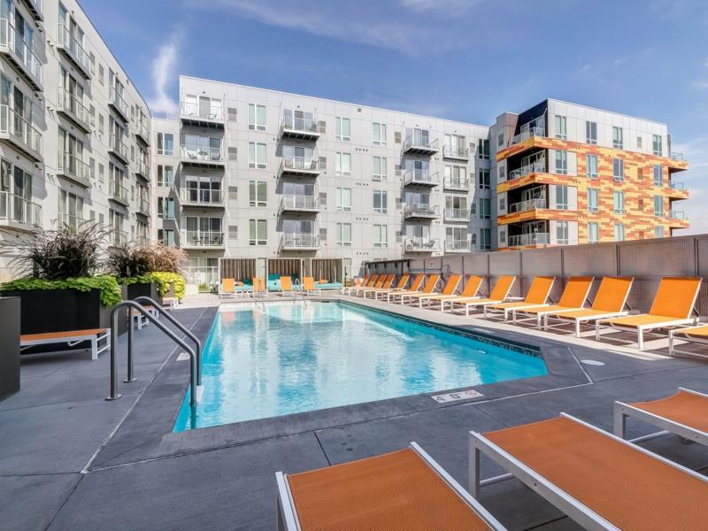 Outdoor swimming pool with lounge chairs and modern apartment buildings in the background.