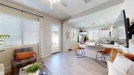 This single-floor residence offers a thoughtfully designed open-concept layout that seamlessly connects the living, dining, and kitchen areas. Light wood-style flooring flows throughout, complementing the warm neutral wall tones that give the entire space a cohesive, modern feel.

The living room is highlighted by vaulted ceilings that amplify the sense of openness, with a ceiling fan overhead and a glass door leading directly to an outdoor patio area. Natural light pours in through large windows dressed with striped drapes, creating a bright and welcoming atmosphere.

The kitchen is well-equipped with white shaker-style cabinetry, light stone countertops, a full suite of stainless steel appliances — including a refrigerator, range, microwave, and dishwasher — and a double basin sink. A peninsula with bar seating provides a casual dining option and further connects the kitchen to the main living area.

The bedroom is a comfortable retreat featuring a ceiling fan, large windows with blinds and curtains, and ample natural light. Artwork and tasteful décor add character to the space.

The bathroom maintains the same clean aesthetic with white cabinetry, stone countertops, wood-style flooring, a glass-enclosed shower, and a window for natural ventilation and light.