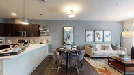Located at 1252 Osgood in North Andover, Massachusetts, this thoughtfully designed single-floor residence offers a seamless blend of modern aesthetics and functional living. The open-concept layout connects the kitchen, dining, and living areas, creating an inviting and cohesive space ideal for both everyday living and entertaining.

The kitchen is a standout feature, showcasing rich dark cabinetry, sleek white quartz countertops, a subway tile backsplash, and a full suite of stainless steel appliances. Open shelving adds a contemporary touch, while pendant lighting above the peninsula provides both task illumination and visual warmth. The adjacent dining area accommodates a round dining table and flows naturally into the living room, which benefits from large windows that invite natural light and offer outdoor views.

The living room features warm hardwood-style flooring, soft neutral wall tones in muted blue-gray, and ample space for comfortable seating arrangements. The bedrooms are carpeted for comfort, with generous natural light from well-proportioned windows. One bedroom features a striking accent wall in a cool slate tone, adding depth and character. The bathroom is well-appointed with dark vanity cabinetry, white countertops, a tub-shower combination with tile surround, and a large vanity mirror.