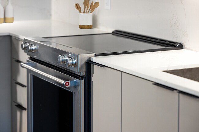 Cocina Signature Collection con gabinetes de color gris claro, estufa eléctrica y encimeras y protector contra salpicaduras de cuarzo marmolado. - Avalon at Becker Farm