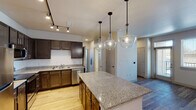 This well-appointed single-floor residence offers a thoughtfully designed open-concept layout that seamlessly connects the kitchen, dining, and living areas. The kitchen is a standout feature, showcasing rich dark-wood cabinetry, granite countertops, and a full suite of stainless steel appliances including a refrigerator, range, microwave, and dishwasher. A central granite-topped island serves as both a prep space and a casual gathering point, while a trio of oversized glass globe pendant lights adds a striking contemporary focal point overhead. Track lighting provides additional illumination throughout the kitchen area. The adjacent dining space benefits from natural light through large windows and a glass door, complemented by durable wood-style flooring that extends through the main living areas. Two carpeted bedrooms offer a comfortable retreat, each featuring windows that bring in natural light and views of the surroundings. One bedroom includes a ceiling fan and a walk-in closet. The unit includes two full bathrooms, each finished with granite-topped dark vanities, wood-style flooring, and tub-shower combinations with clean white tile surrounds. Throughout the space, neutral wall tones and consistent finishes create a cohesive, move-in-ready environment suited for everyday living.