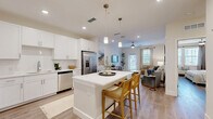 Located at 1023 Gull Ln in Melbourne, FL, this well-appointed one-bedroom, one-bathroom residence offers a thoughtfully designed single-floor layout that maximizes every square foot. The open-concept living area seamlessly connects the living room, dining space, and kitchen, creating an airy, cohesive environment bathed in natural light from large windows. Wood-look flooring flows throughout the main living areas, complemented by neutral tones and recessed lighting with a ceiling fan overhead.

The kitchen is a standout feature, showcasing white shaker cabinetry, stainless steel appliances, a subway tile backsplash, and a white quartz-topped center island with pendant lighting and bar seating — ideal for casual dining or entertaining. The living room opens to a private balcony through a glass-paned door, offering outdoor views of the surrounding landscaped grounds.

The spacious primary bedroom accommodates a generous furniture arrangement and includes two closets, a ceiling fan, and bright windows. The full bathroom features a white vanity with quartz countertop, illuminated mirrors, tile-surround soaking tub, and wood-look flooring. A dedicated laundry area adds everyday convenience. The residence is part of a modern multi-story community with ample parking.
