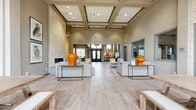 Located at 2450 Oak Hill Cir in Fort Worth, TX, this expansive single-story clubhouse offers a refined and welcoming environment designed for both relaxation and productivity. The grand entrance greets visitors with soaring double-height ceilings, ornate wrought-iron double doors, and large clerestory windows that flood the foyer with natural light, all set atop light-toned tile flooring. The main living area is an open, airy gathering space featuring wood-look tile flooring, a striking floor-to-ceiling stacked stone fireplace, pendant lighting clusters, a built-in wet bar, and a billiards table — creating an inviting social atmosphere. A second, more intimate living space provides a cozy lounge with a gaming and media room decorated in a playful retro arcade theme. The dining area is bathed in natural light from floor-to-ceiling windows with garden views, centered beneath an elegant chandelier. The dedicated office features multiple workstations equipped with computers and a printer, ideal for business needs. Throughout the clubhouse, curated artwork and thoughtful décor enhance the sophisticated yet approachable ambiance. A fitness center is also accessible directly from the main hall, rounding out this well-appointed community space.