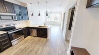 Located at 5001 White Settlement Rd in Fort Worth, TX, this one-bedroom, one-bathroom unit offers a well-designed layout that maximizes its efficient footprint. The open-concept kitchen and living area serves as the heart of the space, featuring rich dark cabinetry, granite countertops, a peninsula with an undermount sink, and a full suite of stainless steel appliances including a refrigerator, range, microwave, and a built-in wine cooler. Stylish pendant lighting over the peninsula adds a modern touch. Wood-style plank flooring flows throughout the main living areas, complementing the clean white walls and bright, airy atmosphere. The living area is bathed in natural light from expansive windows and offers direct access to a private balcony with pleasant outdoor views of surrounding greenery. The bedroom features plush carpeting, a ceiling fan, and a window with natural light, and connects directly to the bathroom for added convenience. The bathroom is well-appointed with dark cabinetry, a framed mirror, a granite-topped vanity, and a full soaking tub with dark tile surround. A dedicated closet provides practical storage. Throughout the unit, the consistent use of dark hardware and cabinetry against light surfaces creates a cohesive, contemporary aesthetic.