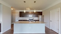 Located at 4890 Edwards Farm Rd in Hilliard, Ohio, this single-floor unit offers a well-designed layout with a thoughtful blend of modern finishes and functional living spaces. The open-concept kitchen serves as a central highlight, showcasing rich dark cabinetry, granite countertops, and a generously sized island with a built-in sink — ideal for both meal preparation and casual dining. Pendant lighting illuminates the island, while a full suite of stainless steel appliances, including a range, built-in microwave, and refrigerator, completes the kitchen. Hardwood-style flooring flows throughout the main living areas and hallways, lending warmth and visual continuity to the space. The living area features a front-facing entry door flanked by large windows that invite natural light and provide views of the surrounding greenery. Bedrooms are finished with plush carpeting and offer windows with outdoor views, creating comfortable, quiet retreats. The bathrooms are well-appointed, with one featuring a granite double-vanity countertop with undermount sinks and a tub-shower combination, while another includes a framed glass sliding shower enclosure. Crown molding and clean white trim throughout add a polished finishing touch to this move-in-ready home.