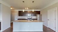 Located at 4890 Edwards Farm Rd in Hilliard, Ohio, this single-floor unit offers a well-designed layout with a thoughtful blend of modern finishes and functional living spaces. The open-concept kitchen serves as a central highlight, showcasing rich dark cabinetry, granite countertops, and a generously sized island with a built-in sink — ideal for both meal preparation and casual dining. Pendant lighting illuminates the island, while a full suite of stainless steel appliances, including a range, built-in microwave, and refrigerator, completes the kitchen. Hardwood-style flooring flows throughout the main living areas and hallways, lending warmth and visual continuity to the space. The living area features a front-facing entry door flanked by large windows that invite natural light and provide views of the surrounding greenery. Bedrooms are finished with plush carpeting and offer windows with outdoor views, creating comfortable, quiet retreats. The bathrooms are well-appointed, with one featuring a granite double-vanity countertop with undermount sinks and a tub-shower combination, while another includes a framed glass sliding shower enclosure. Crown molding and clean white trim throughout add a polished finishing touch to this move-in-ready home.