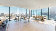 Located in the heart of Detroit at 222 Third Street, this generously scaled, single-floor amenity space offers a sophisticated and modern environment defined by floor-to-ceiling curtain wall glazing that floods every room with natural light and frames stunning panoramic views of the Detroit River, Windsor's Canadian shoreline, and the downtown skyline.

The space comprises two distinct living areas connected by a hallway. The first living area is a bright, open lounge featuring light hardwood flooring, a large mounted display wall with integrated wood paneling, ambient cove lighting beneath a suspended ceiling feature, and ample room for flexible seating arrangements. The second living area offers a more dynamic, recreation-oriented layout with expansive corner glass walls, a ping pong table, casual lounge seating, and direct access to the outdoor terrace through full-height glass doors.

The rooftop terrace is a standout feature, offering an expansive open-air deck with large-format pavers, built-in wood and concrete bench seating, raised planters with greenery, a fire pit, lounge chairs, and glass railings that preserve unobstructed views of the river and cityscape. Wall-mounted exterior speakers enhance the outdoor experience.

Throughout, the design maintains a clean, contemporary aesthetic with neutral tones, exposed concrete columns, and seamless indoor-outdoor connectivity.